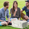closed white picnic basket on grass with three people