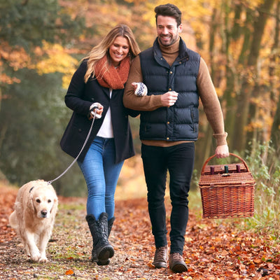 two people walking carrying brown wicker picnic basket
